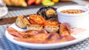 Une assiette de nourriture pour le petit-déjeuner comprenant des saucisses, des tomates grillées, des champignons et des haricots.