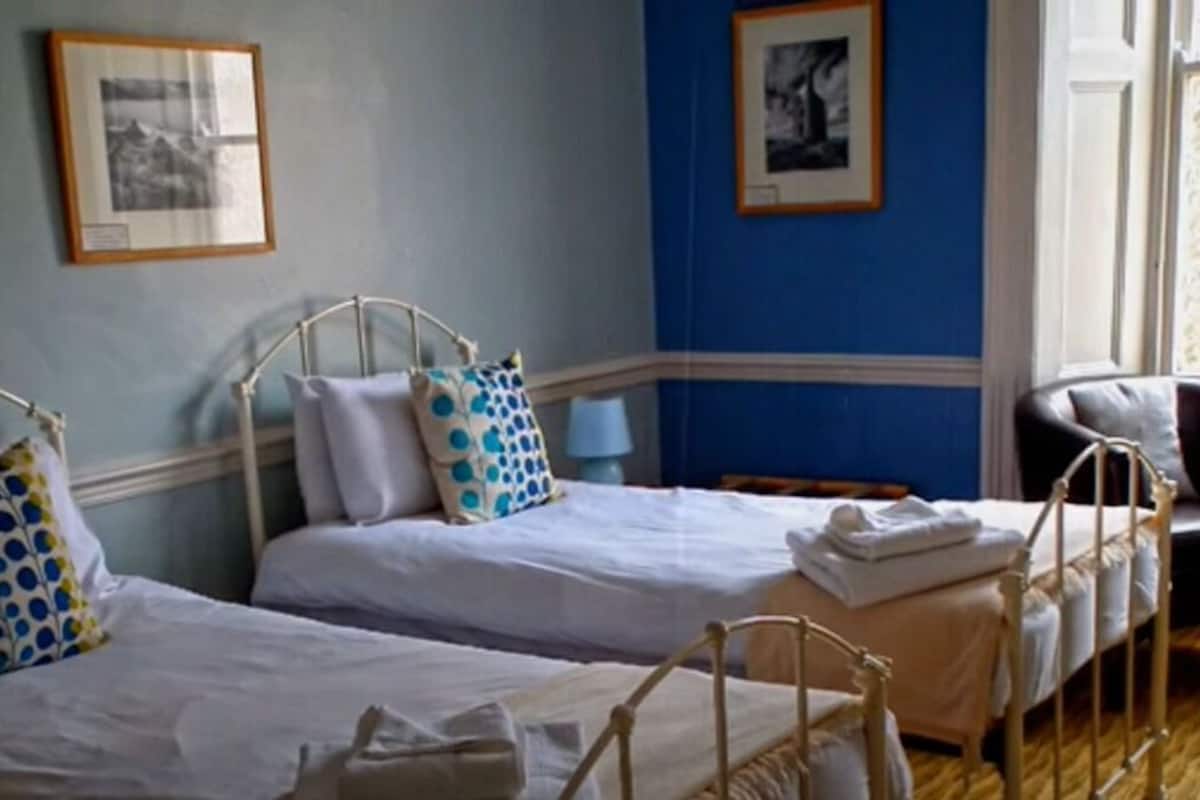 A room with two single beds, a chair, a lamp, and framed pictures on the wall.