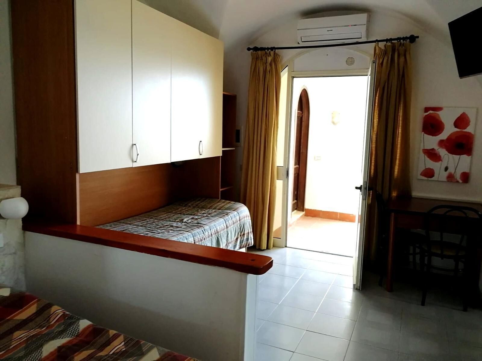 A bedroom with a bed, a wooden headboard, a wardrobe, a desk, and a chair.