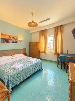 Hotellihuone, jossa on sänky, työpöytä, tuoli, vaatekaappi ja taulu seinällä.