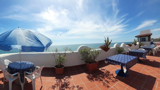 A terrace with outdoor seating, a blue umbrella, and a view of the sea.