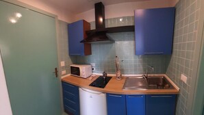 A compact kitchen with blue cabinets, a microwave, a sink, and a dishwasher.