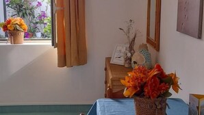 A dining area with a blue tablecloth, a wooden chair, a vase of flowers, and a window with curtains.