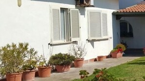 A building with a white facade, terracotta roof tiles, and a small garden area with potted plants.