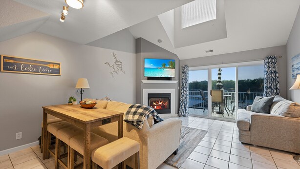 A modern living room with a fireplace, a dining area, and a balcony with a view of the water.