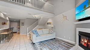 A spacious living room with a high ceiling, a fireplace, and a television mounted on the wall.