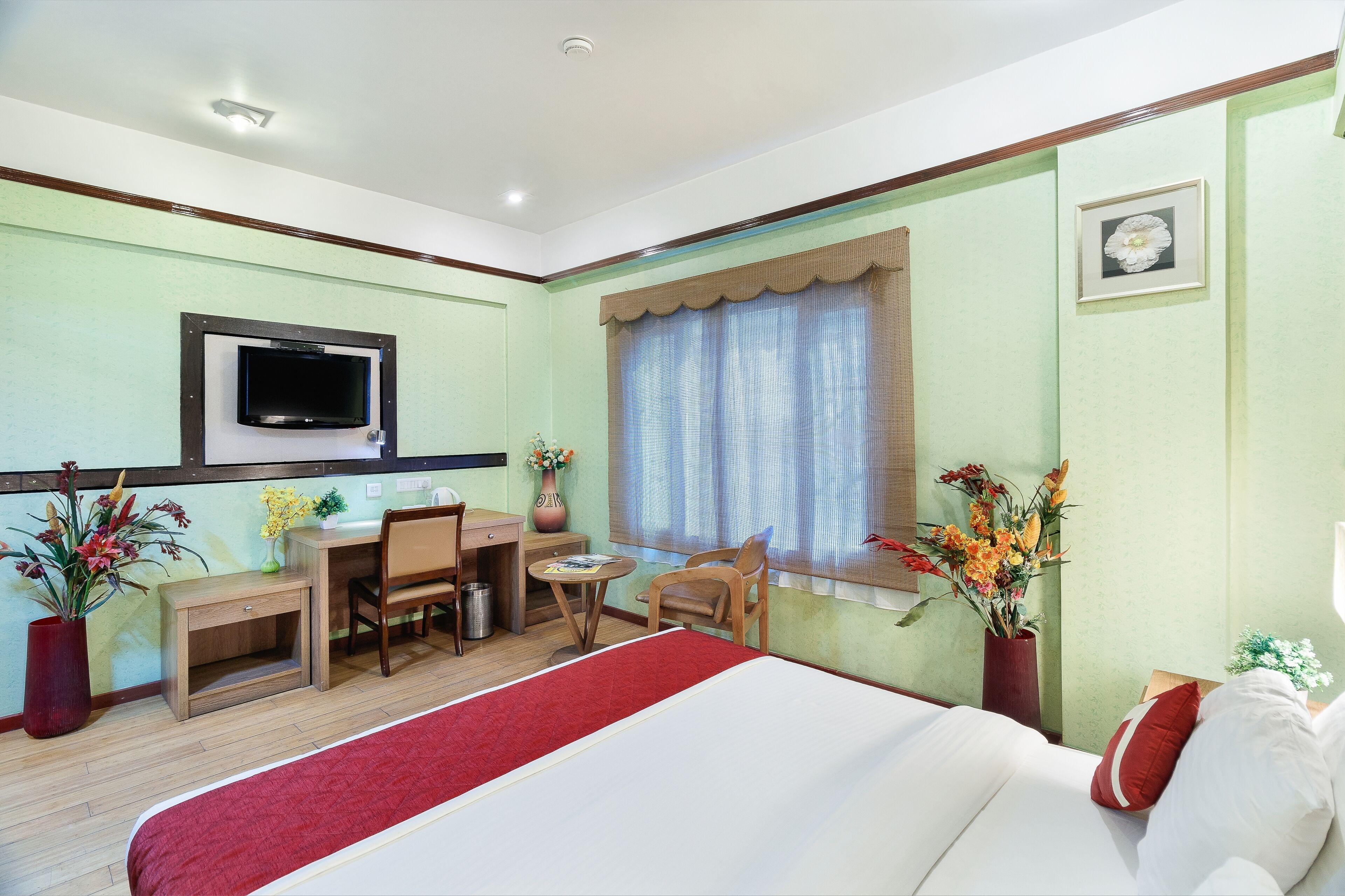 Ein Hotelzimmer mit Bett, Schreibtisch, Stuhl, Fernseher und zwei Blumenvasen.