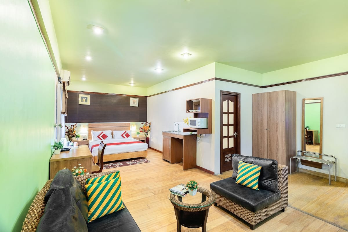 A hotel room with a bed, a desk with a computer, a sofa, a small table, and a wardrobe.