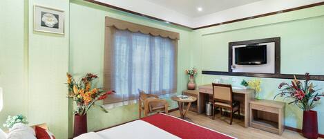 Habitación de hotel con cama, escritorio, silla, televisión y ventana con cortinas.