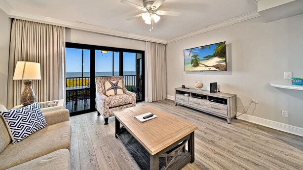 A spacious living room with a large window overlooking the ocean, a ceiling fan, a flat-screen TV, and a wooden coffee table. - Bayside Villa 5236: Bayfront Views! (Captiva)