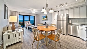 A modern kitchen with stainless steel appliances, a dining area with a round wooden table and chairs, and a living area with a sofa and a lamp. - Bayside Villa 5236: Bayfront Views! (Captiva)