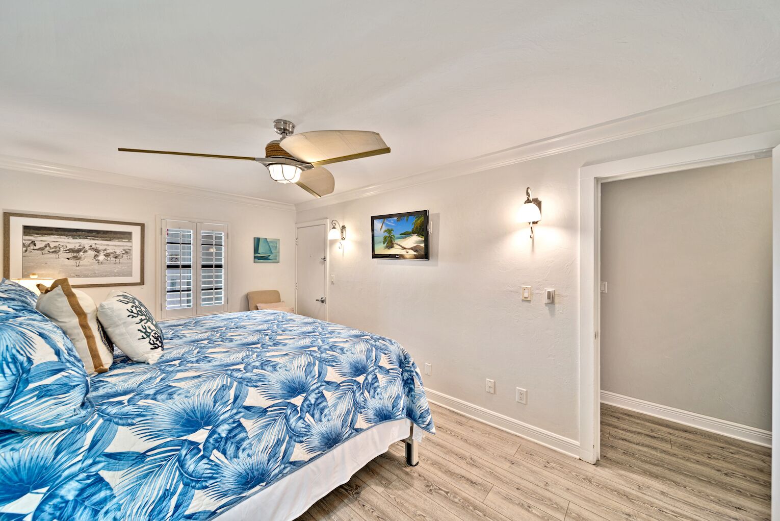 Een slaapkamer met een bed, een plafondventilator, een schilderij en een deur.