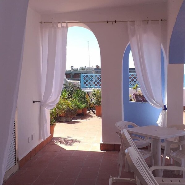 A covered outdoor area with white curtains, a table, and chairs, and potted plants.