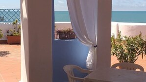 Une terrasse couverte avec vue sur la mer, des chaises blanches et des plantes en pot.