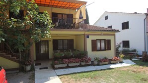 A two-story house with a balcony, a staircase, and a garden with potted plants. - Comfortable apartment Trupec not far from the center. (Malinska)