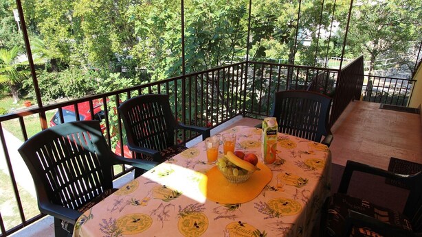 A balcony with a table set for two, featuring a floral tablecloth, two chairs, and a fruit bowl with grapes and peaches. - Comfortable apartment Trupec not far from the center. (Malinska)