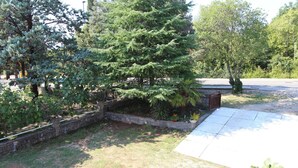 A garden area with a variety of trees, a stone wall, and a paved path. - Comfortable apartment Trupec not far from the center. (Malinska)
