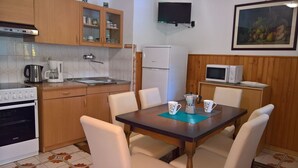 A compact kitchen with wooden cabinets, a stove, a sink, and a microwave. There is a dining table with chairs and a coffee maker on it. - Comfortable apartment Trupec not far from the center. (Malinska)