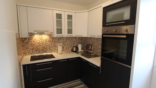 A compact kitchen with white cabinets, a black oven, and a tiled backsplash. - Attractive apartment Janeš Studio for 3 persons on the island of Krk (Sveti Anton)