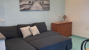 Una habitación con un sofá gris, un armario de madera, una mesita pequeña y un cuadro colgado en la pared que muestra un muelle.
