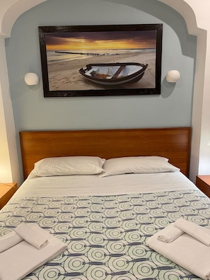 A hotel room with a bed, a wall-mounted picture of a boat on a beach, and two bedside lamps. - Two-room apartment, large terrace, sea front (Camellia) (Anzio)