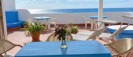 A terrace with a blue table and wicker chairs, overlooking the sea.