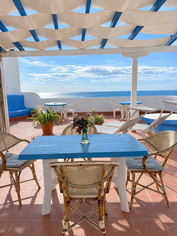 A terrace with a blue table and wicker chairs, overlooking the sea.