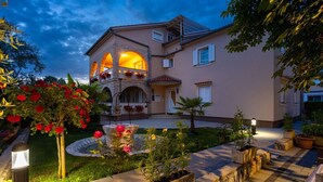 Una casa de dos pisos con un balcón, un jardín con flores y una entrada bien iluminada.