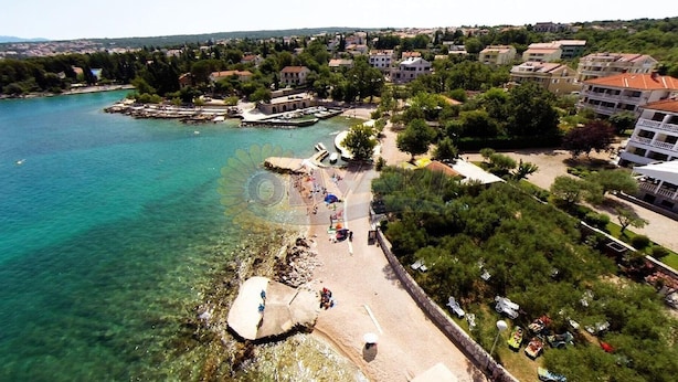 Vista aérea de un pueblo costero con aguas turquesas cristalinas, un paseo marítimo con gente y edificios con balcones.