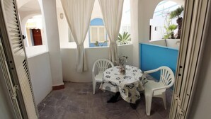 A small patio with a table and chairs, a white door, and a view of a blue building through a window. - Double room, Terrace, No kitchen, Ground floor (Gardenia) (Anzio)