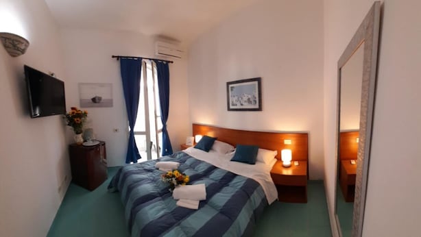 A hotel room with a bed, a bedside table, a nightstand, a TV, a window with curtains, and a framed picture on the wall. - Double room, Terrace, No kitchen, Ground floor (Gardenia) (Anzio)