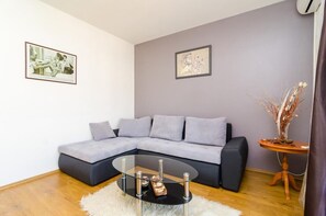 Ein modernes Wohnzimmer mit einem grauen Ecksofa, einem Glastisch und zwei gerahmten Kunstwerken an den Wänden.