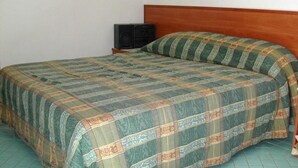A bed with a patterned bedspread, a wooden headboard, and a small black speaker on a nightstand. - Studio, terrace, first floor (Ortensia) (Anzio)