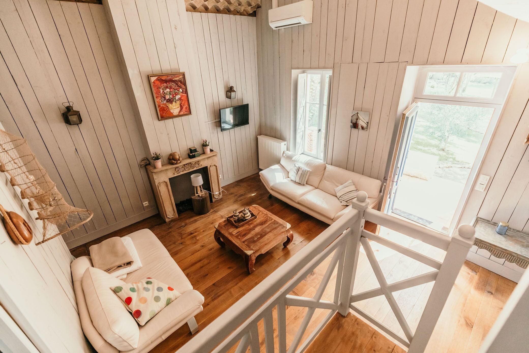 A cozy living room with a wooden floor, white walls, a white sofa, a wooden coffee table, and a fireplace.