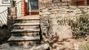 Un bâtiment doté d’un escalier en pierre menant à une porte, d’un porche couvert avec un toit de chaume et d’une fenêtre ornée d’un garde-corps en métal.