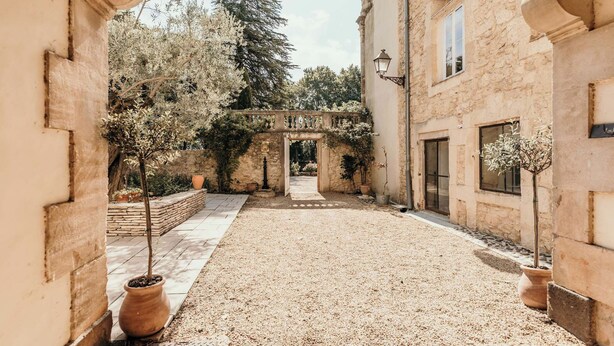 Une cour intérieure agrémentée d’une arche en pierre, de plantes en pot et d’un chemin de gravier.