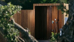 Une cabine de douche extérieure en bois, équipée d’un tuyau d’arrosage et d’un robinet.