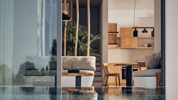 Un salon moderne avec une piscine à débordement en verre, des meubles en bois et une vue sur un bâtiment à l’extérieur.