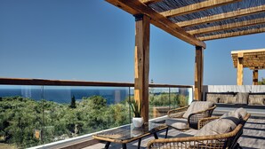 Un balcon agrémenté de meubles en osier, d’une table en verre et offrant une vue sur la mer.