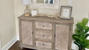 Un mueble de madera con paneles trenzados, un espejo, una lámpara y un cuadro encolado encima.