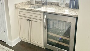 Una cocina con un refrigerador de acero inoxidable, un lavamanos y un ventanal con persianas.
