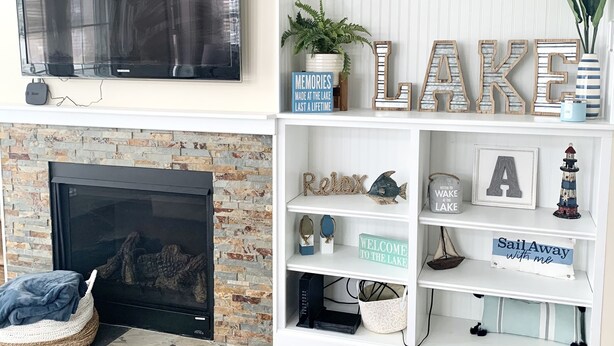 Una sala de estar con chimenea, televisor montado y una estantería blanca decorada con objetos y letreros.