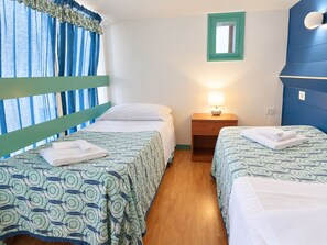A room with two beds, a nightstand with a lamp, a window with curtains, and a mirror on the wall.