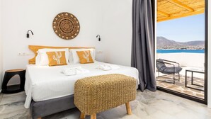 Quarto com cama, um banquinho de fibra natural, vista para o mar e uma varanda com cadeira.