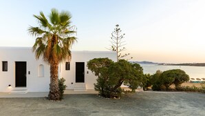 Um edifício branco com uma porta preta, uma palmeira e vista para o mar.