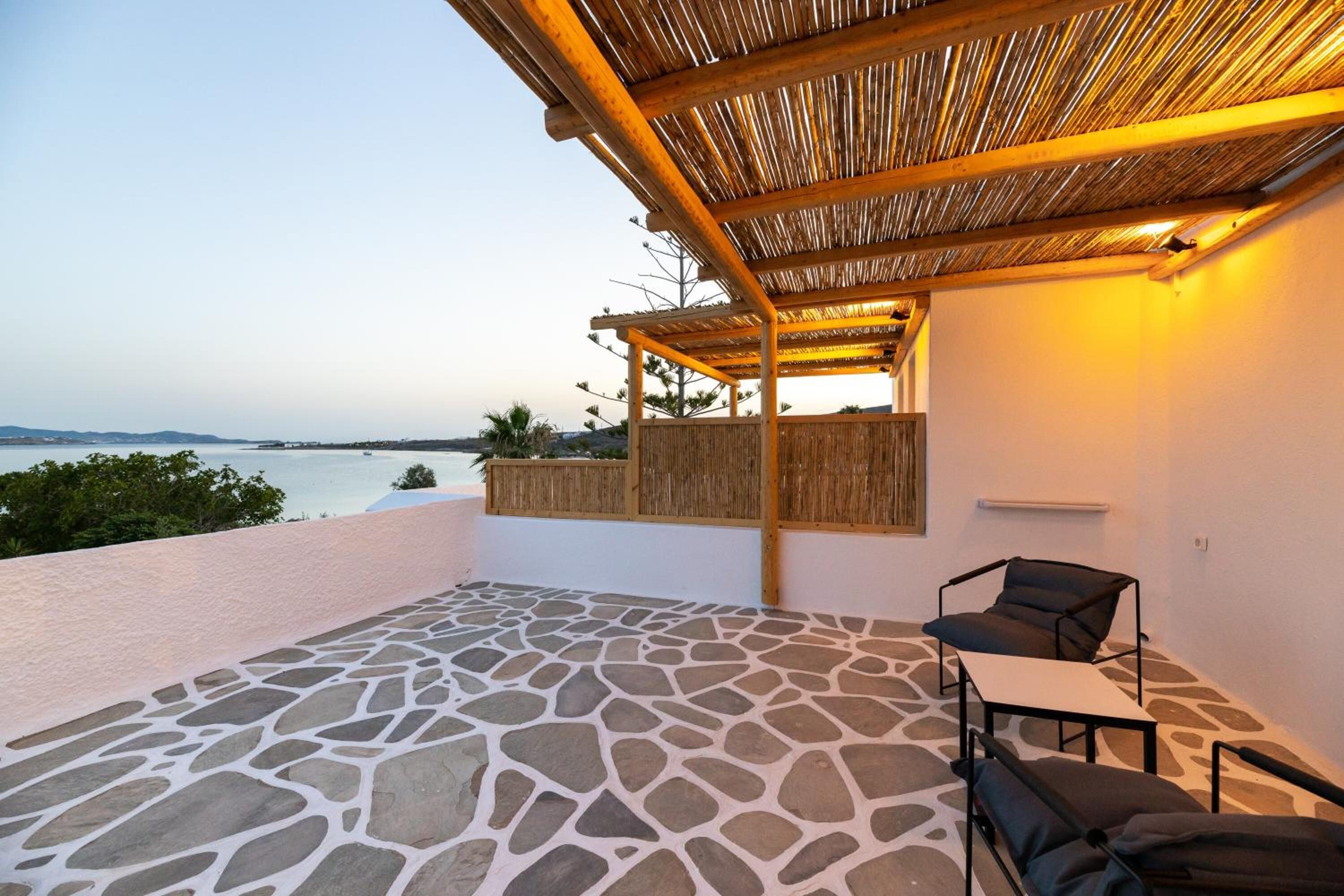 A covered outdoor patio with stone flooring, a seating area with two chairs and a table, and a view of the sea.