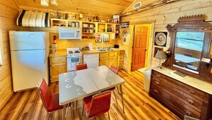 A cozy cabin-style kitchen with wooden walls, a refrigerator, stove, microwave, and a dining area with a table and chairs. - Stone Drive In #305 (Mountain View)