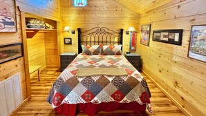 A cozy wooden cabin bedroom with a quilted bedspread, two bedside tables with lamps, and a small window with a view of the sky. - Stone Drive In #305 (Mountain View)
