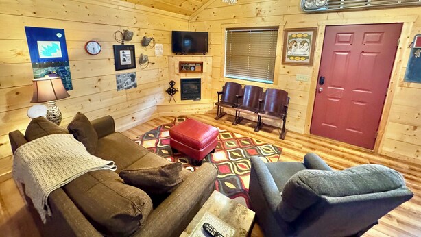 A cozy cabin interior with a wooden ceiling, a television, a fireplace, and a red door. - Stone Drive In #305 (Mountain View)