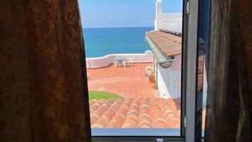 Ein Fenster mit Blick auf eine Küstenlandschaft, darunter ein Gebäude mit rotem Ziegeldach und einem strahlend blauen Himmel.